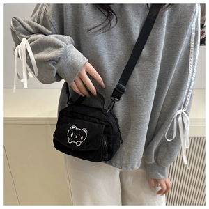 Detail of black corduroy crossbody bag with cute white bear embroidery and strap