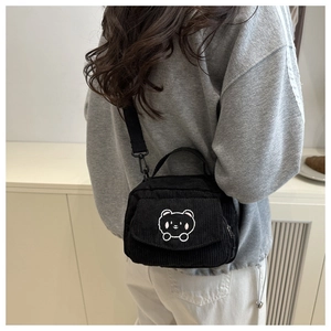 Detail of black corduroy crossbody bag featuring a cute white embroidered bear and shoulder strap