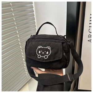 Close-up of black corduroy messenger bag featuring a white embroidered bear pattern