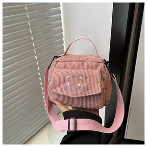 Detail of pink corduroy fabric with purple cartoon bear embroidery on small messenger bag