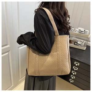 Detail of a beige tote bag showing woven texture and long strap worn over the shoulder