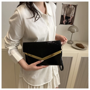 Detail view of black envelope clutch featuring a gold V-shaped metal buckle and textured leather