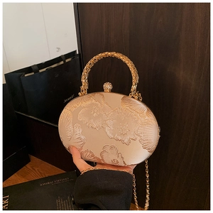 Detalle de bolso de noche champán con bordado floral y elegante asa de anillo oro