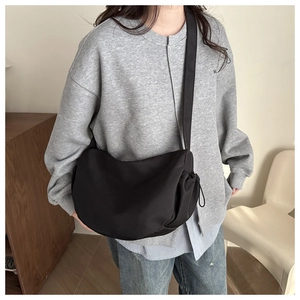 Detail of black nylon half-moon crossbody bag with drawstring design on model