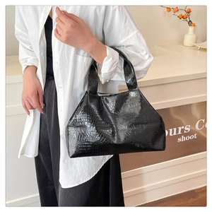 Detail of black glossy crocodile pattern tote bag featuring a wide shoulder strap