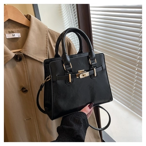 Detail of a black textured handbag featuring a golden turn-lock closure and leather straps