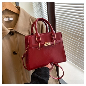 Detail of red glossy Kelly bag with gold metal lock and leather straps on trench coat