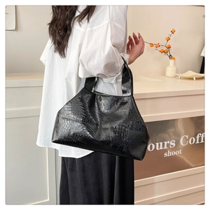Detail of black crocodile pattern tote bag held by a model in a minimal white shirt