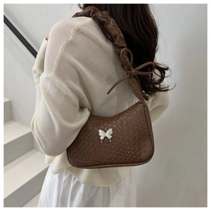 Sac bandoulière tissé marron avec papillon blanc et sangle froncée porté par un mannequin