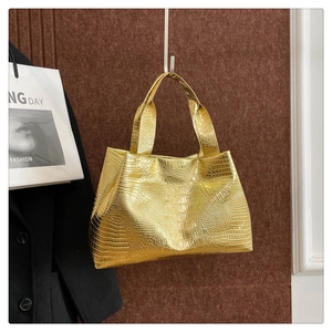Detail of gold tote bag with crocodile pattern texture and metallic finish handles