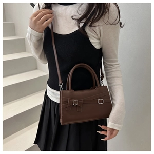 Detail of dark brown leather crossbody bag with silver hardware and bow on white stairs