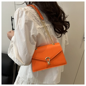 Detail of orange crocodile-patterned chain bag with metallic U-shaped buckle on model