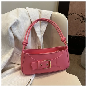 Detail of pink underarm bag featuring decorative wide strap and gold metal buckle on a chair
