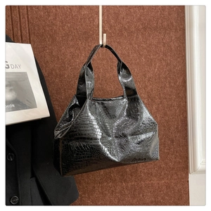 Detailed close-up of a glossy black crocodile pattern tote bag hanging on a brown wall