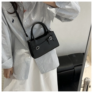 Detail of black matte leather square bag with decorative buckle bow and top handle