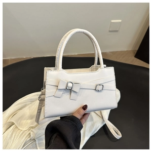 Close-up of white leather handbag featuring a stylish bow and silver buckle detail