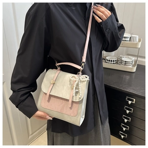Detail of gray and pink patchwork crossbody bag with pearl bow charm and top handle