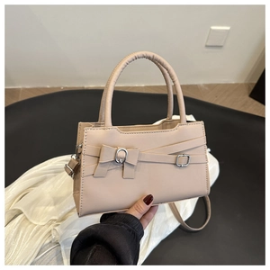 Detail of beige rectangular handbag with cross strap, bow design and silver metal buckle