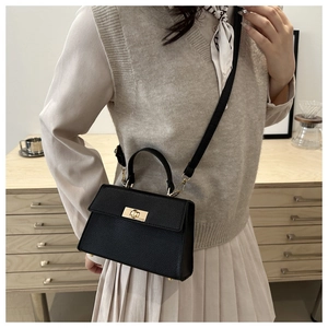 Detail of black lychee grain leather crossbody bag with a gold twist lock on wooden desk