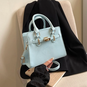 Light blue Kelly style handbag with gold lock shown with black blazer and books
