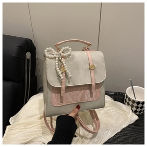 Close-up of a grey leather backpack with pink trim and a large pearl bow charm detail