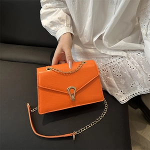 Vibrant orange chain shoulder bag with crocodile pattern and golden buckle on white lace dress
