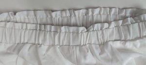 Detailed view of white pleated elastic waistband with paperbag ruffle trim and fine stitching