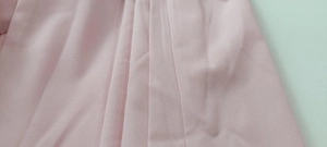 Detail of light pink pleated fabric showing texture and vertical fold design of the jumpsuit