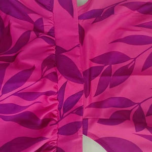 Dettaglio del tessuto dell'abito fucsia con stampa di foglie viola e trama arricciata