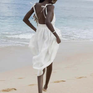 Elegant white backless maxi dress with thin straps flowing in the ocean breeze