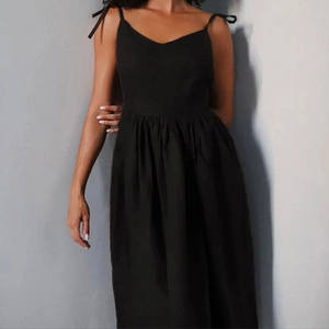 Detail of black V-neck sleeveless dress with bow straps and pleated waistline