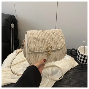 Detail of beige straw saddle bag with floral embroidery and gold metal buckle