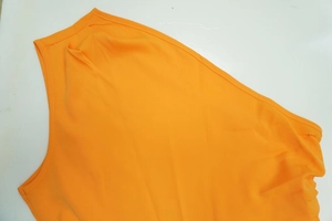Detailed macro view showing the neckline and stitching of an orange one-shoulder jumpsuit.