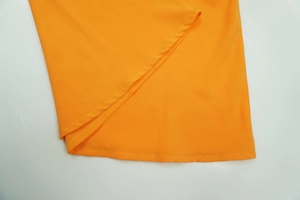 Detailed close-up of the high-quality hem stitching on bright orange wide-leg jumpsuit