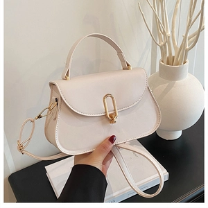 Close-up of cream leather handbag with gold oval clasp and detachable shoulder strap