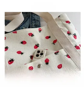Detalle del bolso de pana con fresas que muestra el bolsillo frontal con móvil y broche