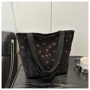 Detalle de bolso tote de pana negra con estampado de fresas y bolsillos laterales