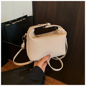 Detail van crème-witte geweven kussentas met goudkleurige hardware en schouderband