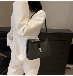 Close-up of a black minimalist underarm bag with silver twist lock on white sweatshirt