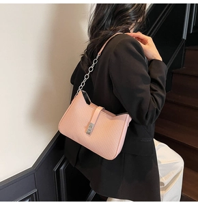 Detail of pink shoulder bag with textured surface and gold chain strap on model