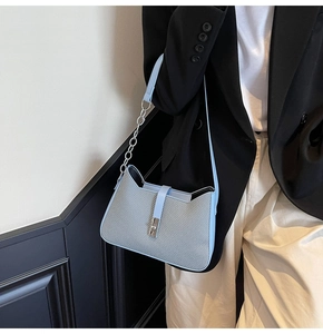 Detail of light blue crossbody bag featuring silver chain and textured grey panel