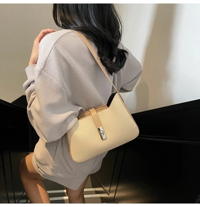 Detail of minimalist cream woven underarm bag with brown leather trim and silver clasp