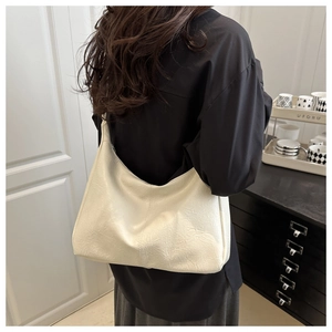 Grand sac bandoulière beige en cuir plissé en forme de croissant porté par un mannequin