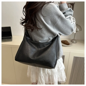 Détail du sac hobo plissé noir en similicuir porté par un mannequin en tenue décontractée