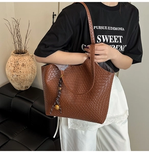 Detail of dark brown woven tote bag with gold ball charm and dual shoulder straps