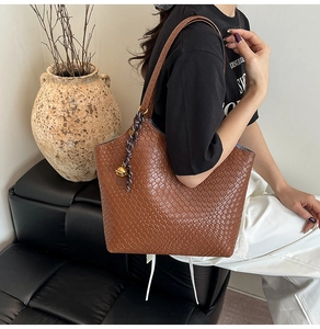 Detail of a brown woven leather tote bag with unique bell charm and shoulder straps