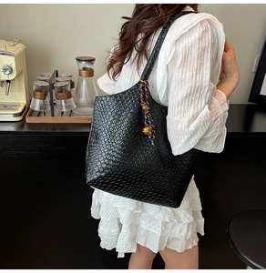 Detail of black woven leather tote bag with elegant metallic ball charm and shoulder strap