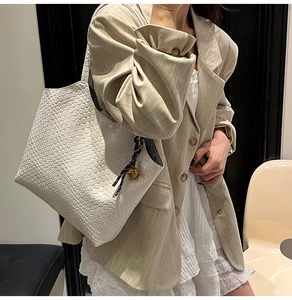 Close-up of white woven tote bag with intricate checkered texture and a bell charm