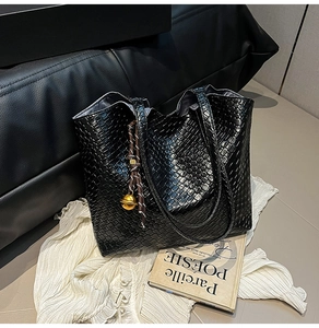 Detail of black woven leather tote bag with gold bell charm and large capacity interior