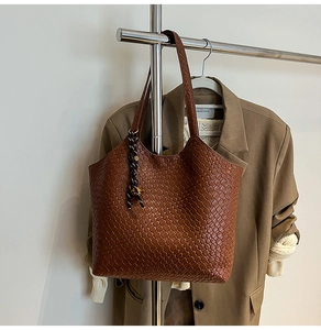 Detail of brown woven tote bag with a striped cord pendant on a metal rack